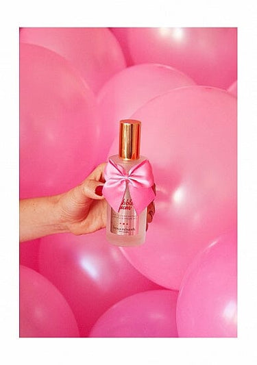 a person holding a bottle of perfume in front of a bunch of balloons